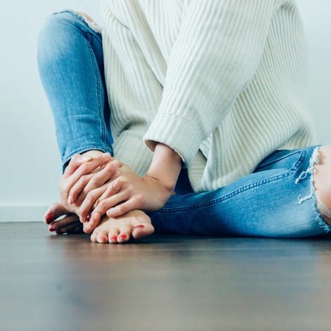 Mädchen mit zerschlissenen Jeans sitzt auf dem Boden. Jeans im Used Look schaden in der Herstellung der Umwelt. Geht das auch nachhaltig? (Foto: unsplash/Imani Bahati)