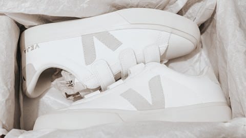In einem Schuhkarton liegen ein Paar weiße Sneaker von der nachhaltigen Marke Veja. Die nachhaltigen Sneaker haben ein graues Veja-Logo an der Seite (Foto: Unsplash/SJ)