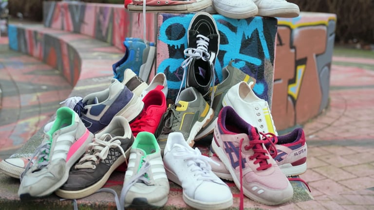 Mehrere Sneaker von Marken wie Vans, Adidas, Nike und Veja liegen auf einem Haufen auf einer mit Graffiti besprayten Mauer. (Foto: SWR)