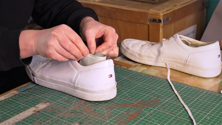 Ein Stück dünnes Leder wird von der Besitzerin einer Schuhreparatur-Werkstatt an den Fersenteil eines Sneakers geklebt. (Foto: SWR)