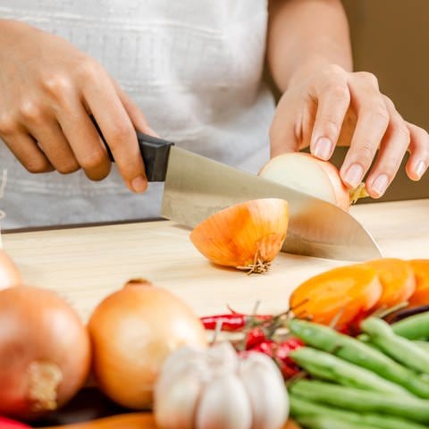 Gute und scharfe Messer sind ein Muss in jeder Küche. Woran erkennt man langlebige Kochmesser? Und ist Preis gleich Qualität? Eine Frau schneidet eine Zwiebel auf einem Küchenbrett. (Foto: Colourbox)