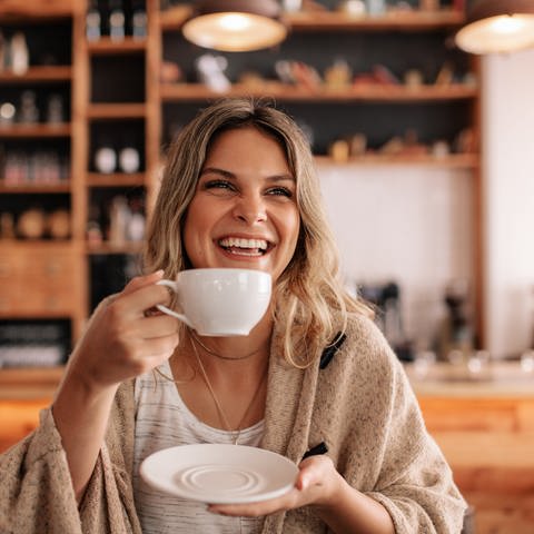 Eine Frau lächelt während sie eine Tasse Kaffee in der Hand hält. (Foto: Adobe Stock, Adobe Stock/Jacob Lund)