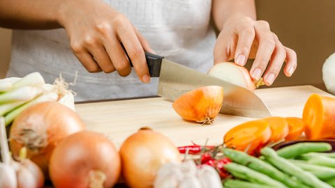 Frau schneidet Zwiebel auf einem Küchenbrett. Gesundes Gemüse mit Geschmack.