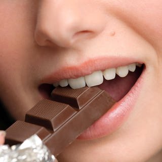 Junge Frau beisst genussvoll von einer Schokolade ab (Foto: imago images, Imago)