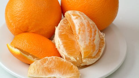 Orangen,Orangenschalen und geschälte Orangen liegen auf einem Teller (Foto: IMAGO, Niehoff)