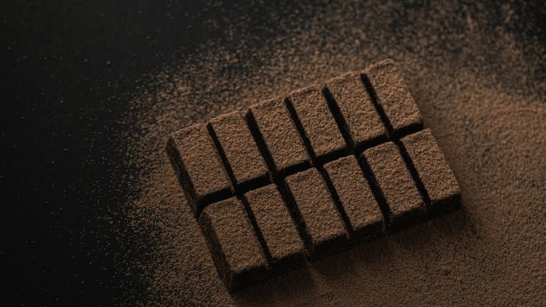 Eine Tafel dunkle Schokolade mit Kakaopuder überstäubt (Foto: IMAGO, wirestock)
