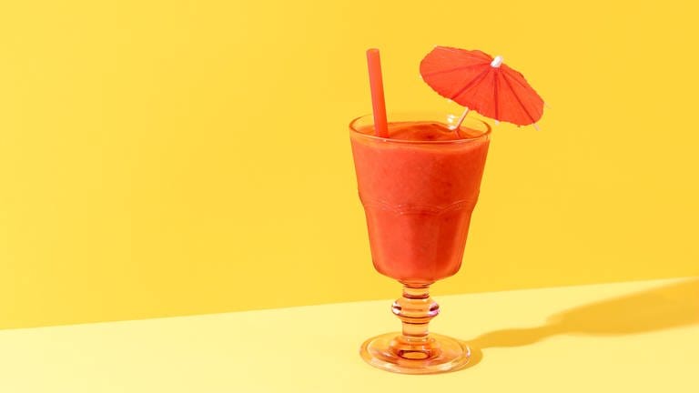 Glas mit roter, dicker flüssigkeit und Schirmchen auf gelbem Hintergrund. Erdbeeren konservieren: Rezept für Erdbeer-Limes (Foto: Colourbox)