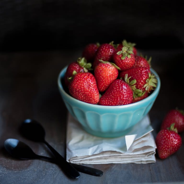 Erdbeeren liegen vor dunklem Hintergrund in einer blauen Porzellanschale. Wie kann man Erdbeeren konservieren? (Foto: unsplash / Anna Ogiienko)