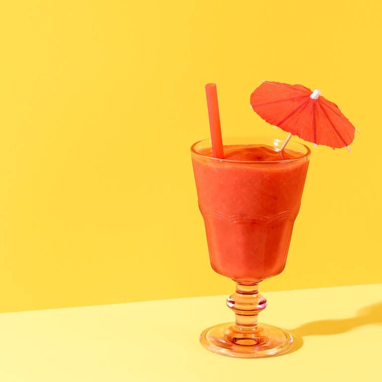 Glas mit roter, dicker flüssigkeit und Schirmchen auf gelbem Hintergrund. Erdbeeren konservieren: Rezept für Erdbeer-Limes