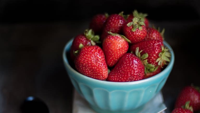 Erdbeeren liegen vor dunklem Hintergrund in einer blauen Porzellanschale. Wie kann man Erdbeeren konservieren?