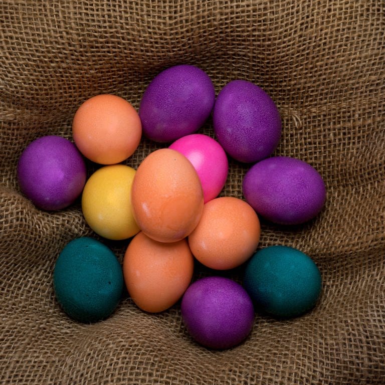 Mehrere bunte Eier liegen auf Sackleinen