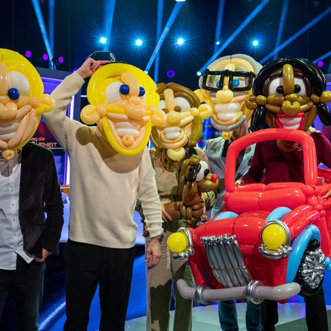 Der Moderator und das Rateteam mit aus Luftballons geformten Masken vor den Gesichtern. Sowie ein Hund und ein Auto aus Luftballons geformt. (Foto: SWR)