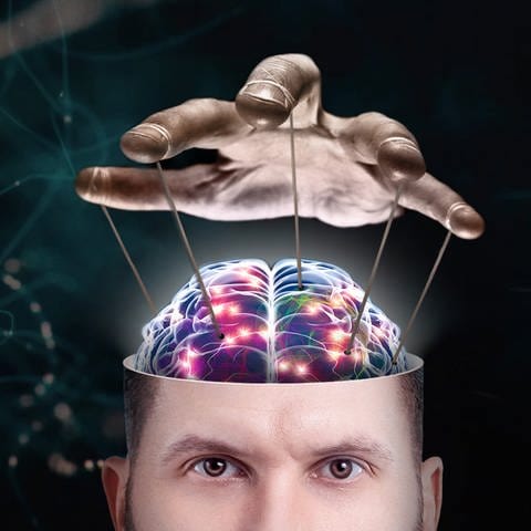 In der unteren Bildhälfte: ein angeschnittener offener Männerkopf, in dem ein Gehirn zu sehen ist. Über dem Gehirn ist eine Hand, die mit Fäden das Gehirn zu steuern scheint – als wäre das Gehirn eine Marionette. Im Bildhintergrund zeichnen sich Nervenzellen ab.