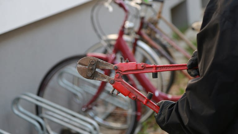 Bolzenschneider in der Hand eines Diebes vor einem Ständer mit Fahrrädern. Gute Fahrradschlösser können vor Fahrraddiebstahl schützen.