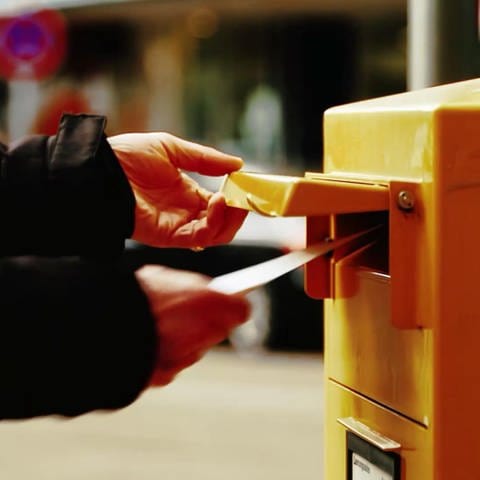 Nahaufnahme von einer Person, welche einen Brief in einen Briefkasten der Deutsche Post wirft