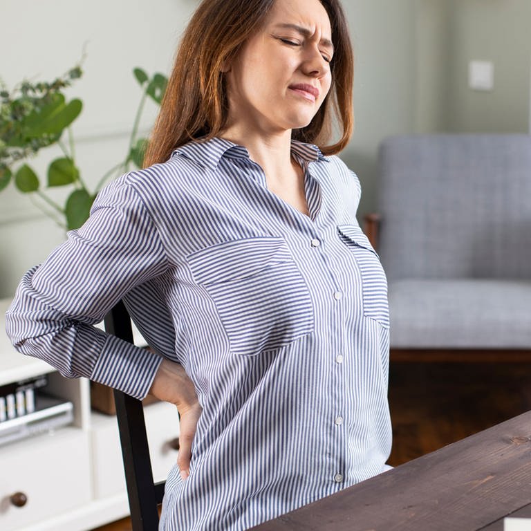 Eine Frau sitzt mit Rückenschmerzen am Schreibtisch