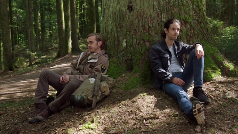 Sebastian und Albert sitzen an einen Baum gelehnt im Wald