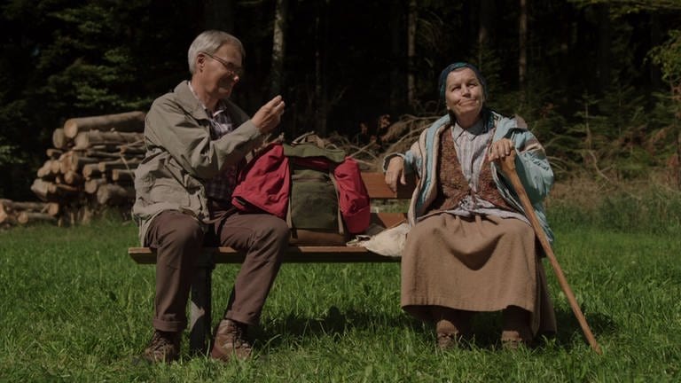 Lioba und Karl sitzen auf einem Bänkle am Waldrand