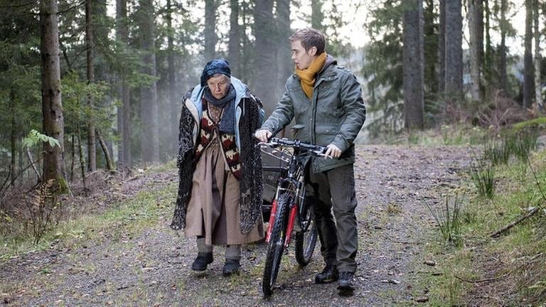 Lioba ist mit Sebastian, der sein Fahrrad schiebt, im Wald unterwegs