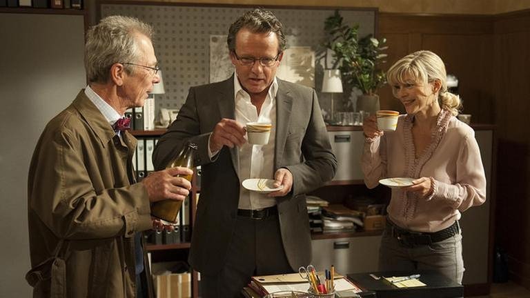 Herr Weiss, Bernhard und Frau Heilert trinken im Bürgermeisterbüro Kaffee