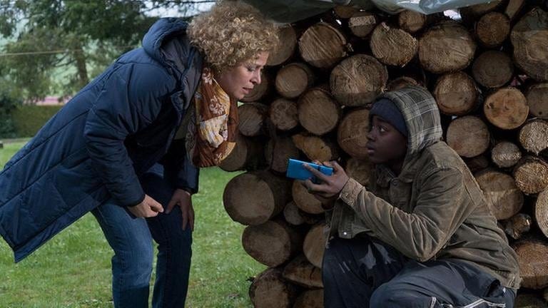 Bea findet Tayo hinter dem Holzstapel, Tayo zeigt ihr etwas auf seinem Handy
