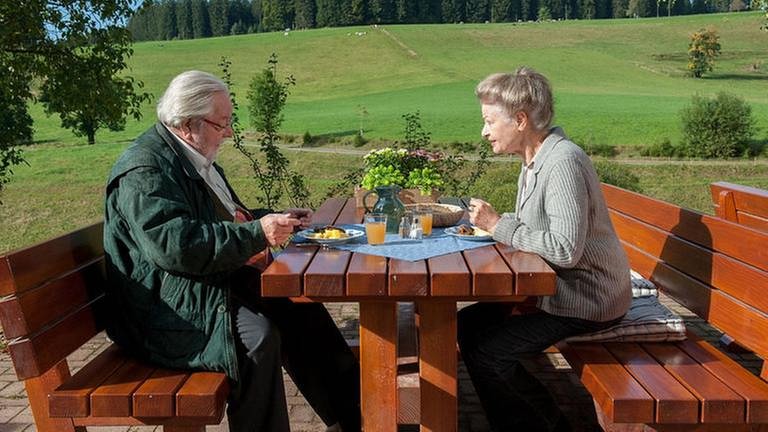 Hermann und Johanna essen auf den Bänken hinterm Hofladen