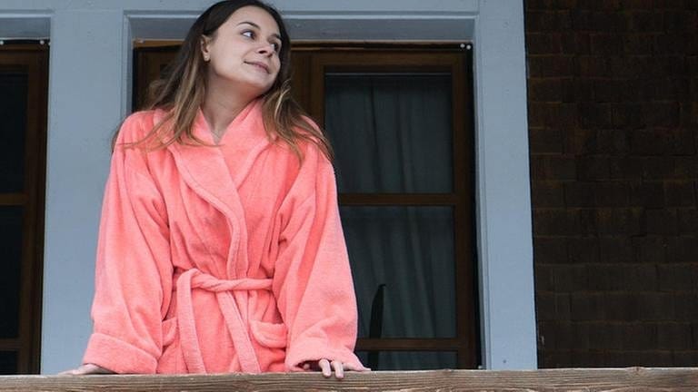 Jenny steht im rosa Bademantel auf dem Balkon