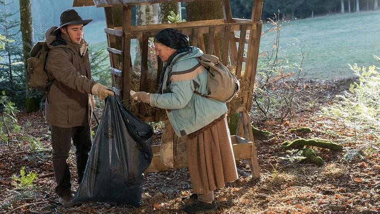Lioba und Sebastian bei einer Futterstelle im Wald, sie sammeln Müll