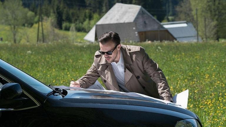 Constantin studiert eine Landkarte, die auf der Motorhaube seines Autos liegt