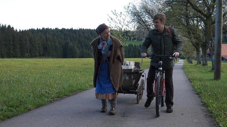 Lioba zieht einen Leiterwagen hinter sich her, Sebastian geht neben ihr mit seinem Fahrrad