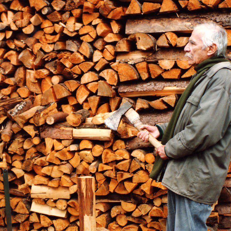 Franz und Wilhelm stehen vor einer Wand mit aufgeschichtetem Brennholz