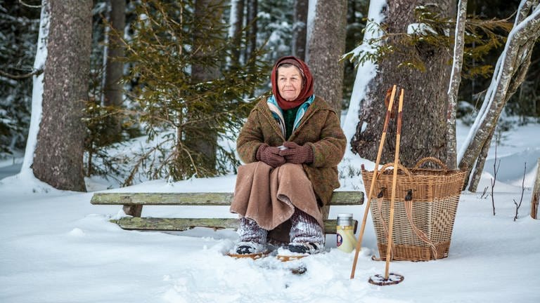 Lioba sitzt im Winter auf einer Bank am Waldrand