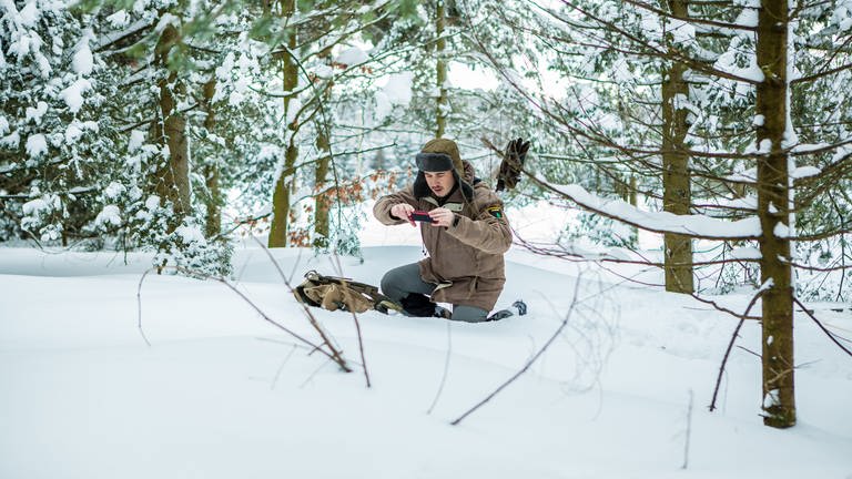 Sebastian kniet im verschneiten Wald und macht ein Foto mit seinem Handy