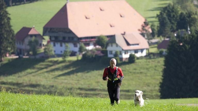 Karl joggt über die Wiese, im Hintergrund der Fallerhof