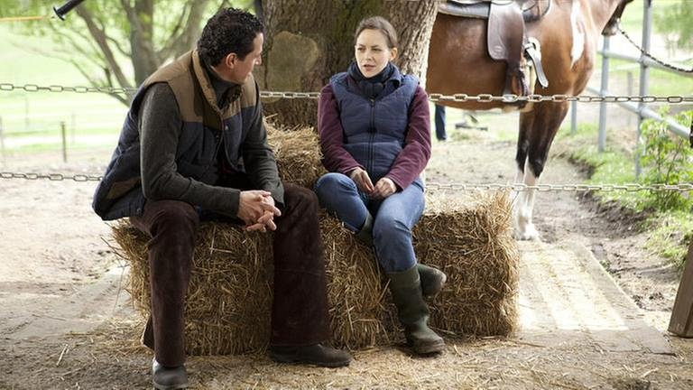 Matthias und Sophie sitzen auf einem Strohballen, im Hintergrund ein Pferd