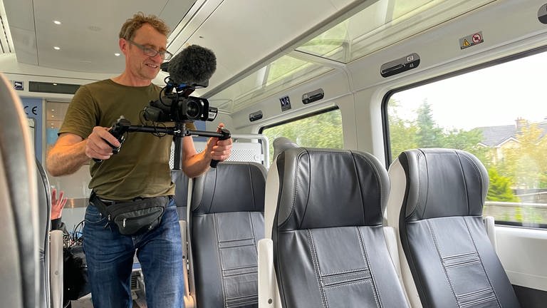 Der Kameramann ist drehbereit. In Zügen ist es oft komfortabler, mit kleineren Kameras zu arbeiten. Man stößt nicht überall an, und wenn der Zug mal wackelt, kann das einfacher ausgeglichen werden. 