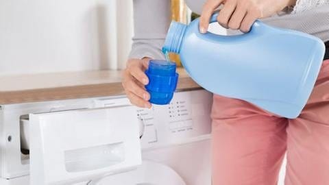 Eine Frau steht vor einer Waschmaschine und gießt Waschmittel in einen Behälter.