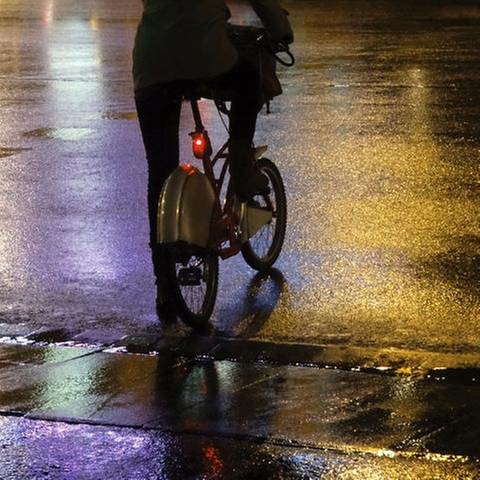 Ein Fahrradfahrer hält nachts auf einer schwach beleuchteten Straße. Sein Rücklicht gibt einen schwachen Schein ab.