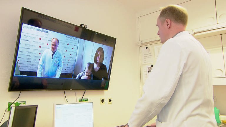 Arzt vor LED-Bildschirm, während einer Telemedizin-Sitzung mit einer Patientin