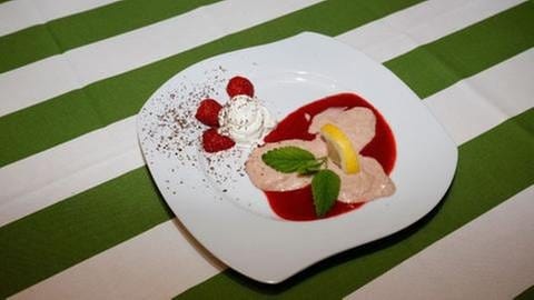 Rhabarbermousse auf Erdbeersauce mit Sahne, Erdbeeren, Minze und Zitronenscheibe dekoriert
