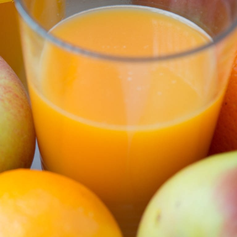Ein Glas mit Fruchtsaft aus einer Flasche steht inmitten von Äpfeln und Orangen.