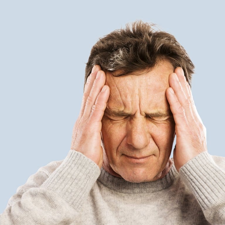 Mann fässt sich an den Kopf. Kopfschmerzen sind ein Schlaganfall-Symptom.