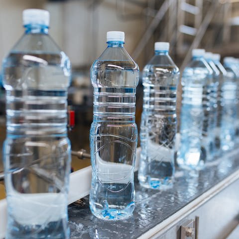 Hintereinander stehen Wasserflaschen aus Plastik auf einem Lieferband in einer Trinkwasserabfüllanlage.