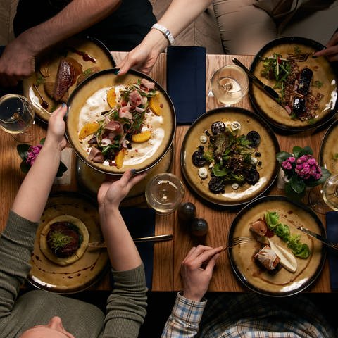 Tisch mit hübsch angerichteten Speisen von oben, drumherum sitzen Menschen und trinken Wein. Weihnachtsmenü: Nachhaltig, regional, einfach und preisgünstig