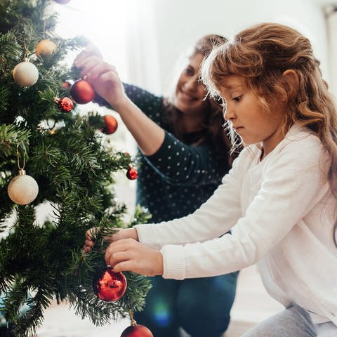 Kleines Mädchen schmückt Weihnachtsbaum. Wie stark sind Tannenbäume mit Pestiziden belastet? Marktcheck macht den Test (Foto: Adobe Stock, Adobe Stock | Jacob Lund)