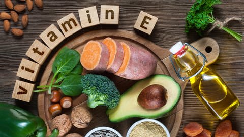 Zu sehen sind verschiedenste Lebensmittel mit Vitamin E Gehalt: Süßkartofeln, Spinat, Öl, und Nüsse.