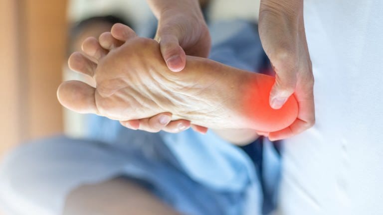 An einem Fuß ist die Fußsohle an der Ferse rot markiert, dort wo der Patient Schmerzen hat. Viele leiden an einer entzündeten Fußsohlensehne und Fersensporn. Wieder schmerzfrei laufen: einfache Übungen und Therapien ohne Operation. (Foto: Adobe Stock)