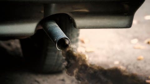 Aus einem Auto-Auspuff kommt schwarzer Rauch. Es handelt sich um CO2-Abgase.