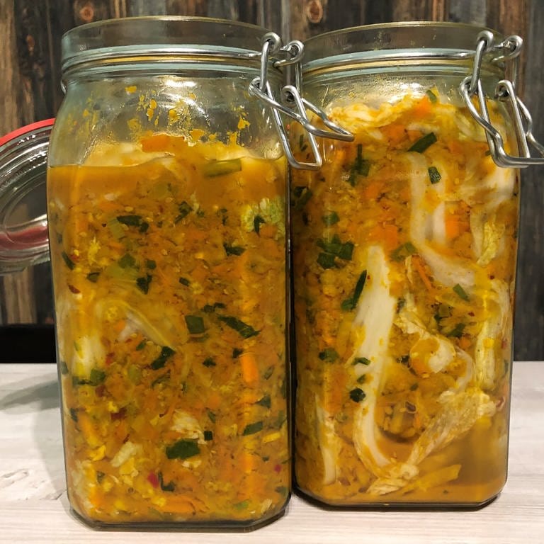 Zwei Drahtbügelgläser mit frisch eingelegtem Kimchi stehen offen zum Fermentieren