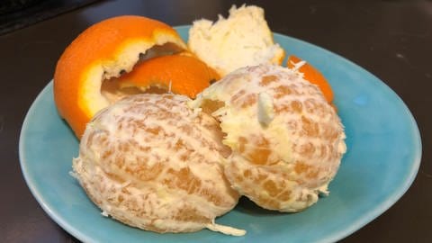 Geschälte Orange mit der Schale auf einem Teller